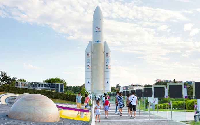 Visitors walking towards a rocket exhibit at Cité de l’Espace, France.