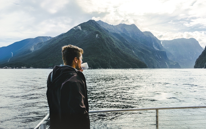 Person enjoying a drink on a Milford Sound cruise with mountain views.