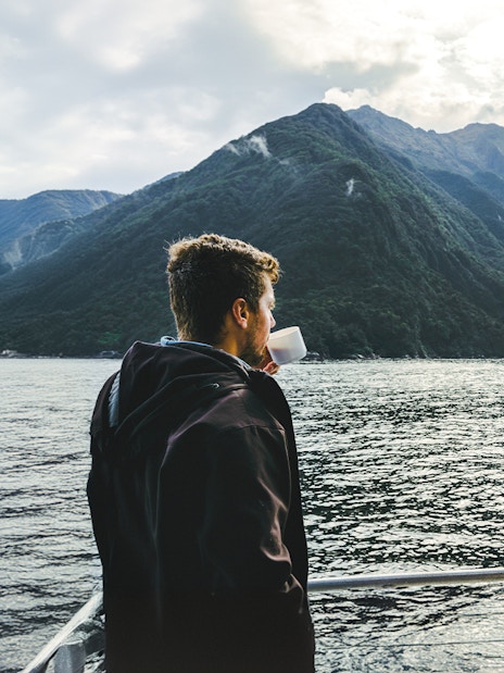 Person enjoying a drink on a Milford Sound cruise with mountain views.