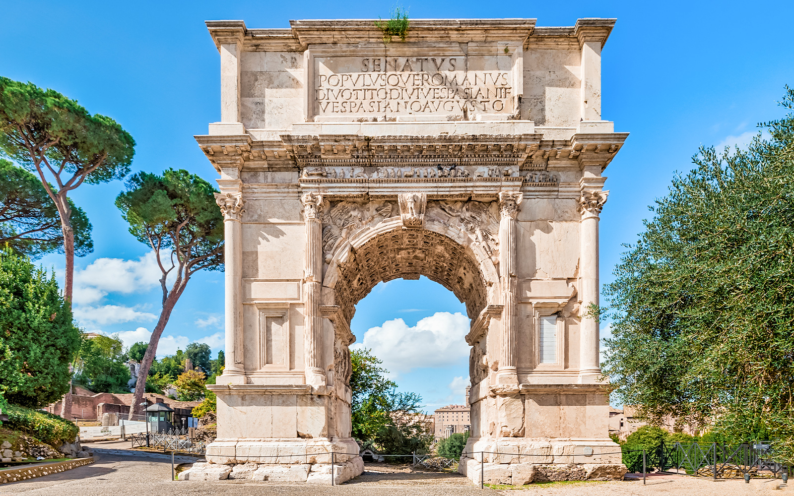 Arch of Titus with trees and blue sky in the Roman Forum, Rome, Italy.