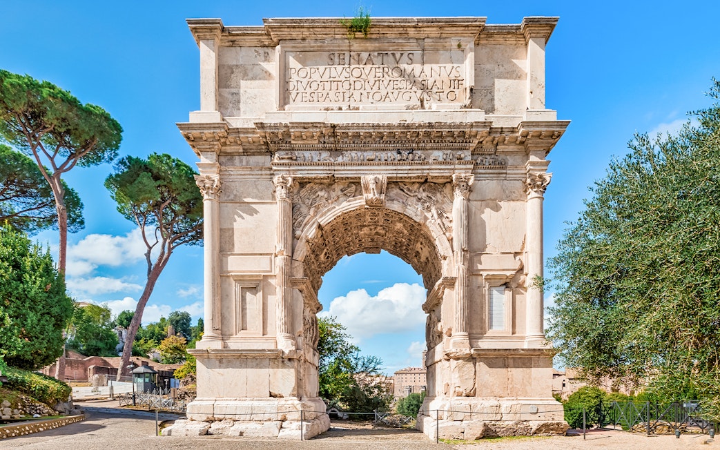 Arch of Titus with trees and blue sky in the Roman Forum, Rome, Italy.