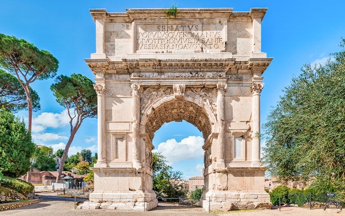 Arch of Titus with trees and blue sky in the Roman Forum, Rome, Italy.