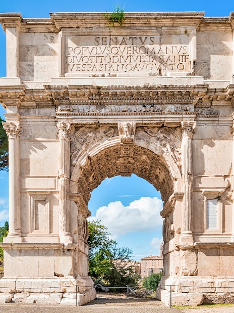 Arch of Titus with trees and blue sky in the Roman Forum, Rome, Italy.