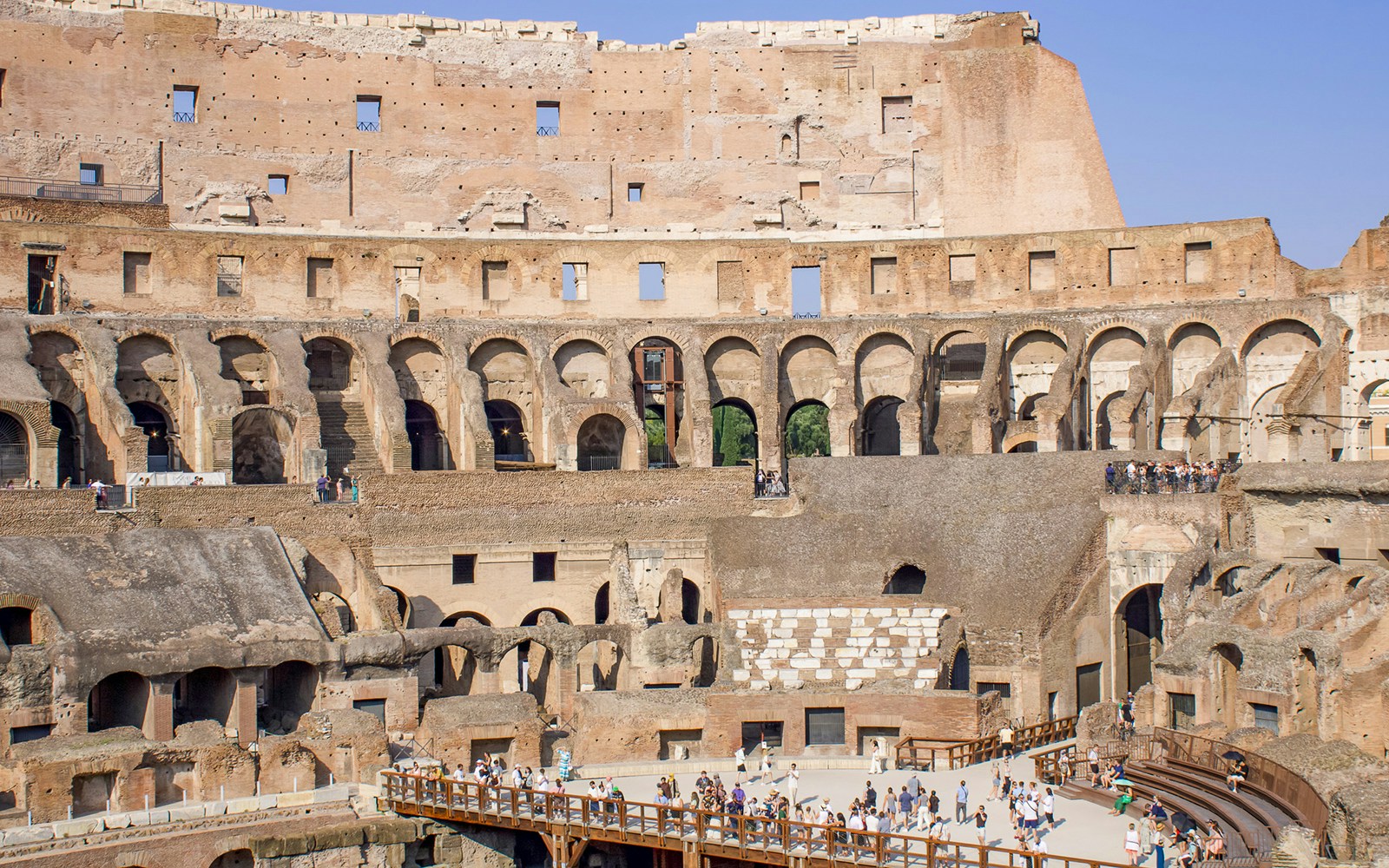 Panoramic view of the Colosseum interior with tourists exploring ancient arches.