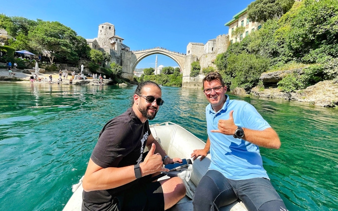 Guests on a boat near Mostar Bridge, Bosnia, with the historic arch in the background.