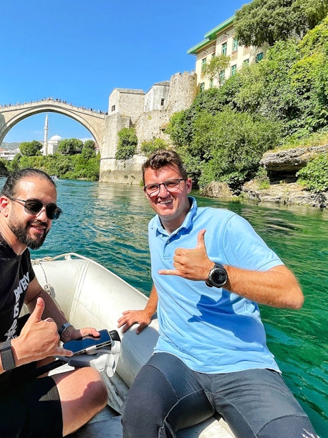Guests on a boat near Mostar Bridge, Bosnia, with the historic arch in the background.
