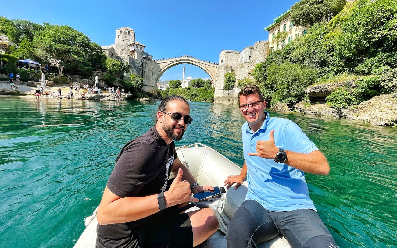 Guests on a boat near Mostar Bridge, Bosnia, with the historic arch in the background.