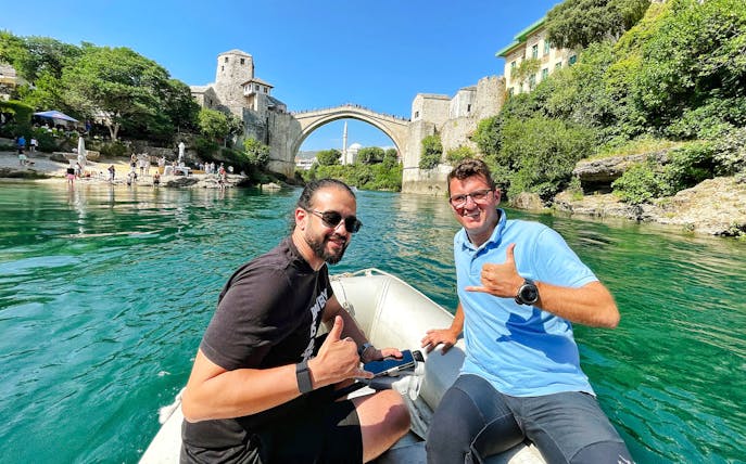 Guests on a boat near Mostar Bridge, Bosnia, with the historic arch in the background.