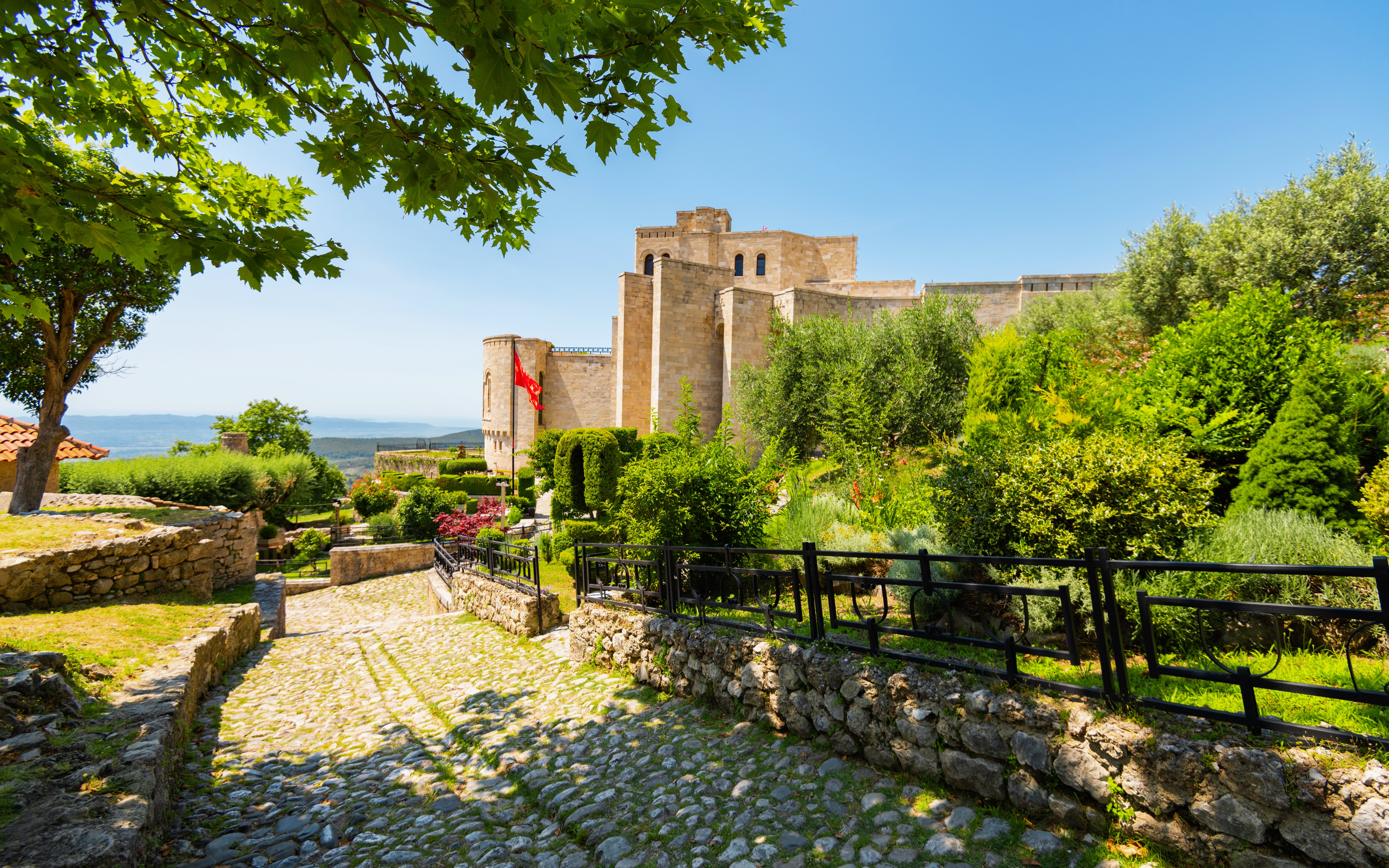 Kruja Castle surrounded by lush greenery under a clear summer sky in Albania.
