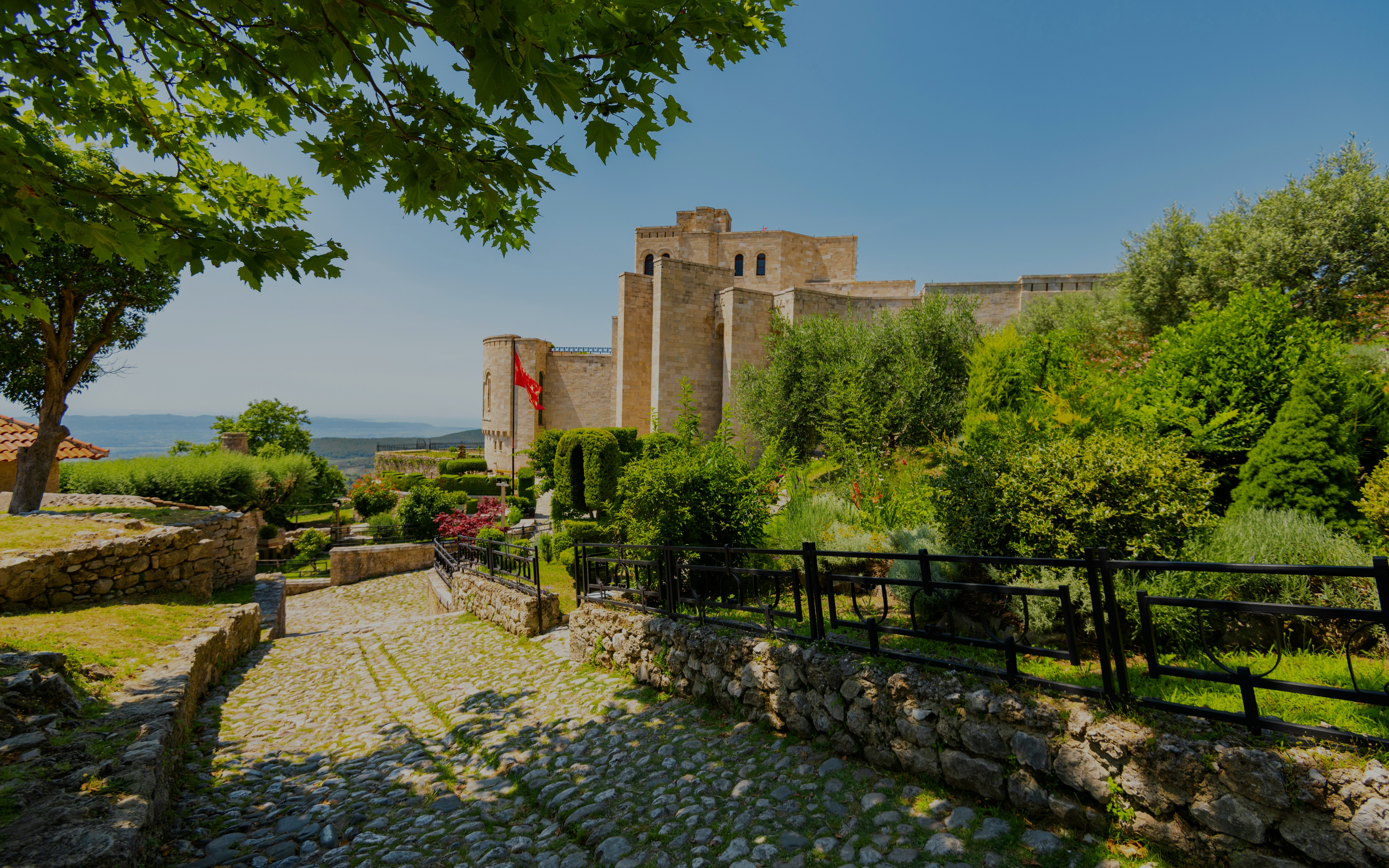 Kruja Castle surrounded by lush greenery under a clear summer sky in Albania.