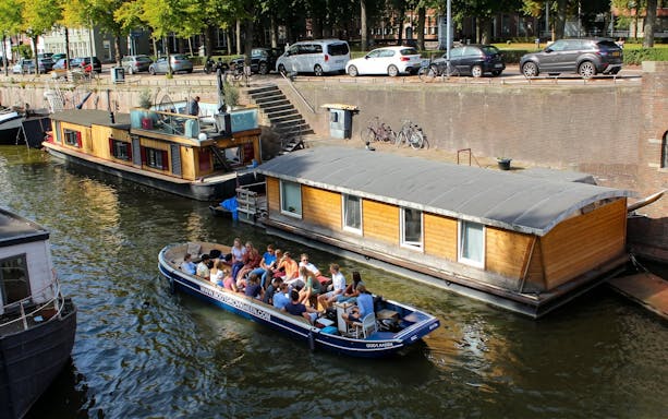 Groningen canal cruise boat with tourists passing houseboats.