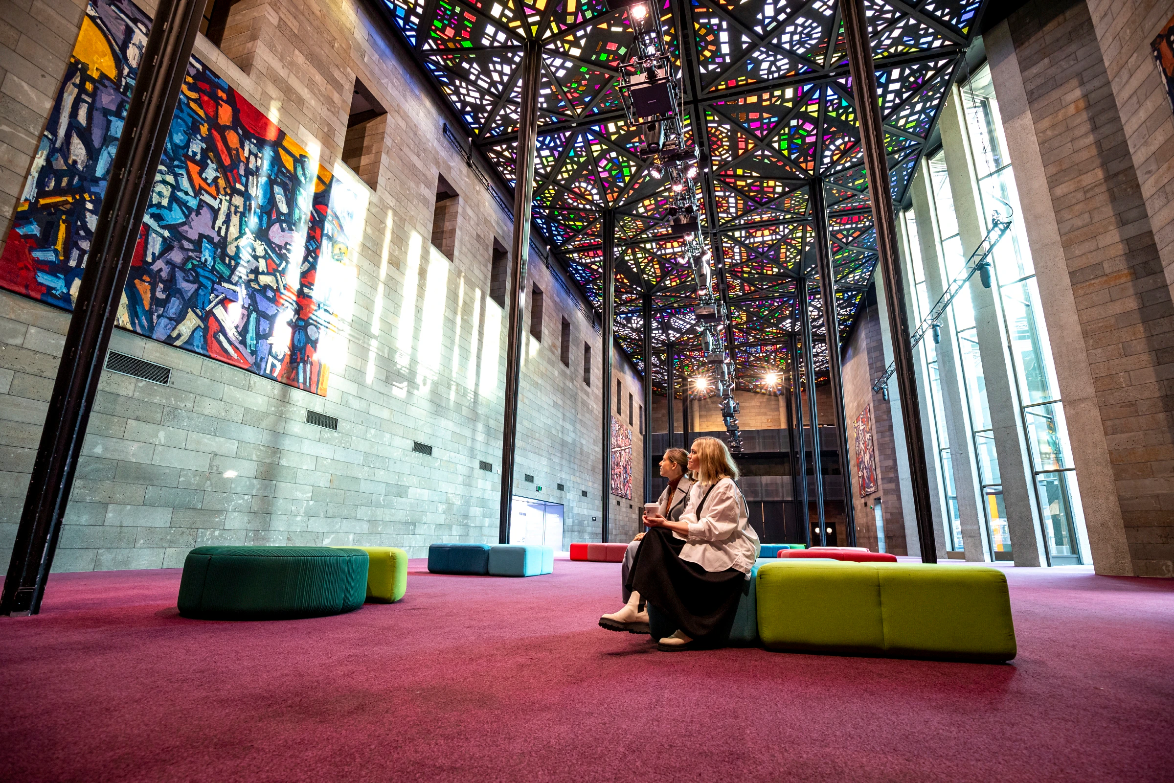 Visitors seated in the Great Hall at NGV International, Melbourne, under a stained glass ceiling.