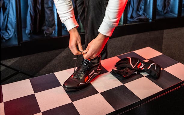 Person tying go-karting shoes on checkered floor with gloves nearby.