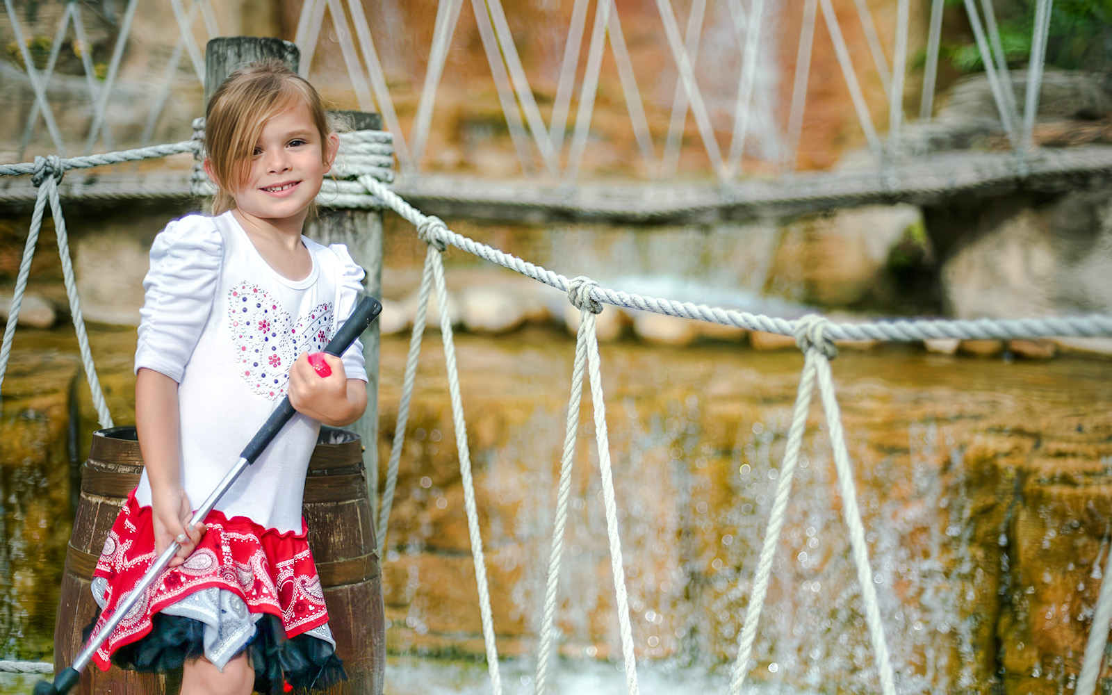 Child holding a mini-golf club at Pirate's Cove Adventure Golf with rope bridge in background.