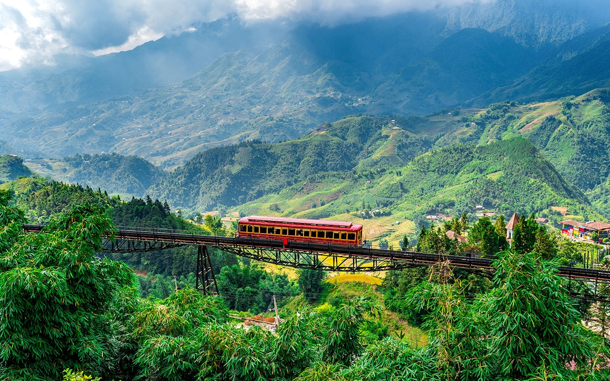Red train crossing a bridge with Fansipan mountain landscape at Sun World Fansipan Legend, Vietnam.