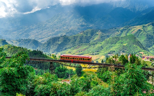 Red train crossing a bridge with Fansipan mountain landscape at Sun World Fansipan Legend, Vietnam.