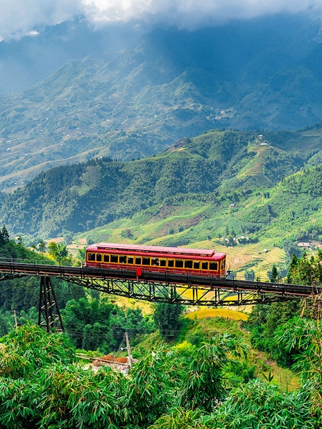 Red train crossing a bridge with Fansipan mountain landscape at Sun World Fansipan Legend, Vietnam.