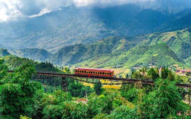 Red train crossing a bridge with Fansipan mountain landscape at Sun World Fansipan Legend, Vietnam.