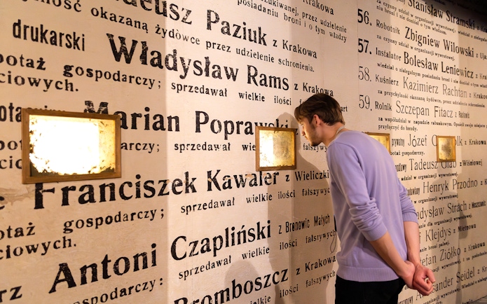 Man examining exhibit wall at Oskar Schindler's Factory museum in Krakow, Poland.