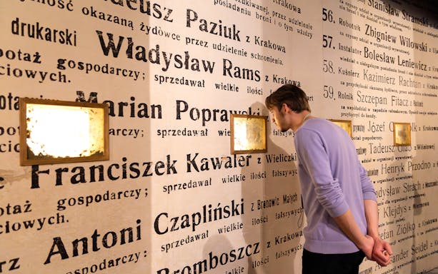 Man examining exhibit wall at Oskar Schindler's Factory museum in Krakow, Poland.