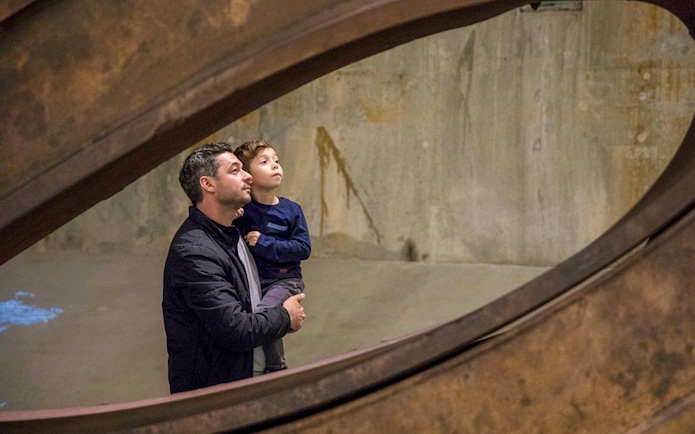 Father and child observing steel beam exhibit inside 9/11 Memorial.