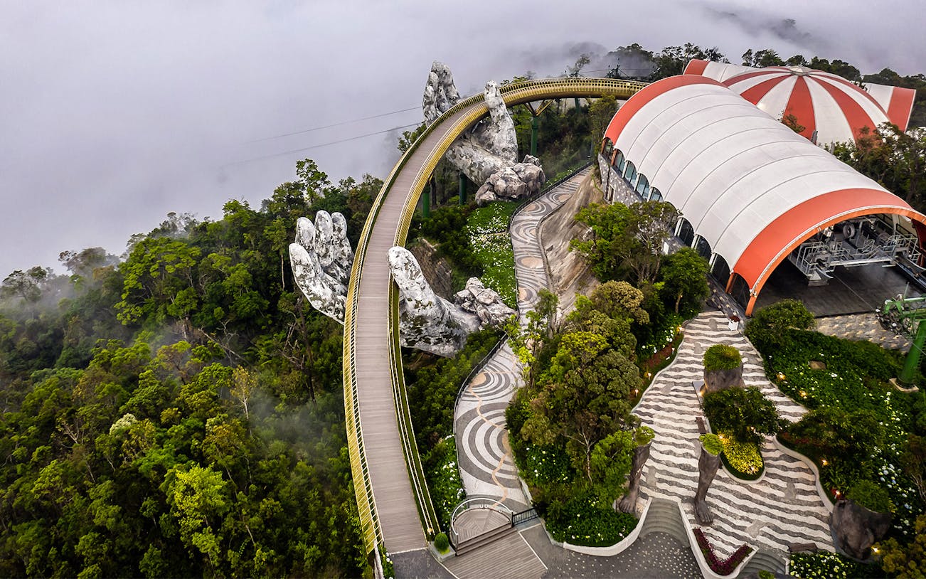 Golden Bridge in Ba Na Hills, Vietnam, held by giant stone hands amidst lush greenery.
