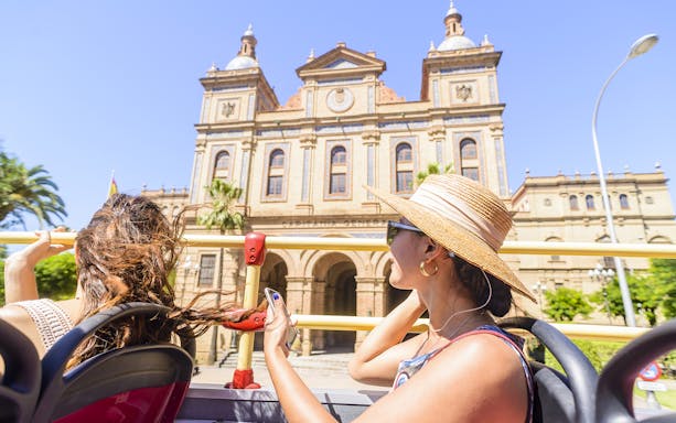 Tourists on Seville hop-on hop-off bus passing historic building.