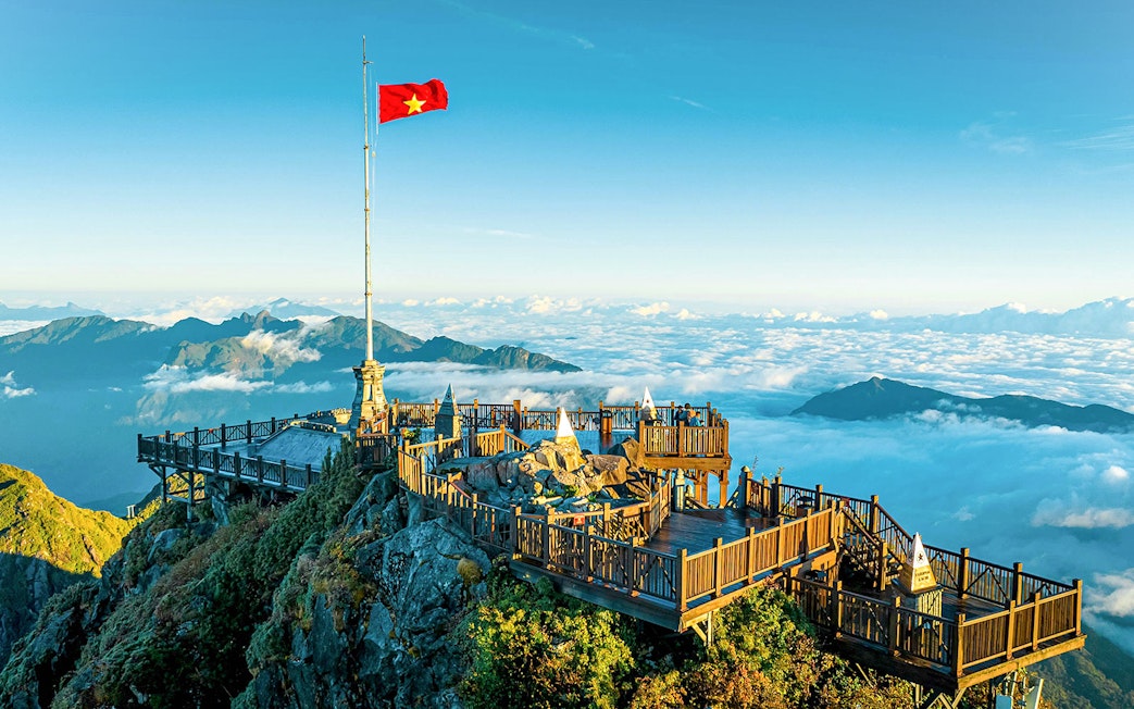 Viewing platform at Sun World Fansipan Legend with Vietnam flag, surrounded by clouds and mountains.