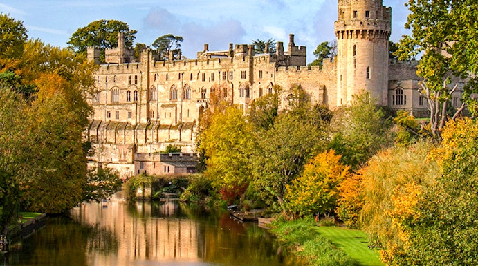 Warwick Castle with river reflection and autumn trees in Warwick, England.