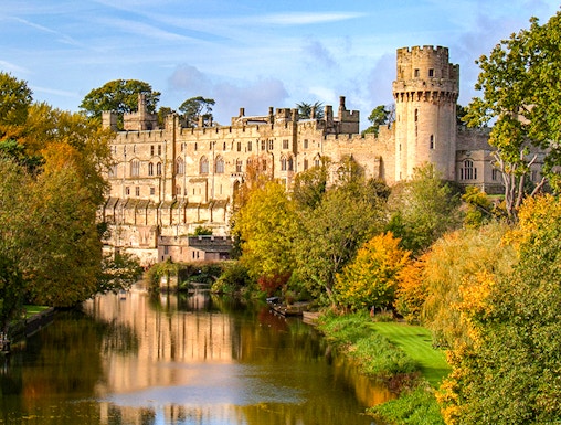 Warwick Castle with river reflection and autumn trees in Warwick, England.