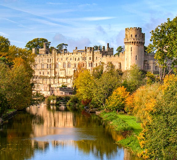 Warwick Castle with river reflection and autumn trees in Warwick, England.