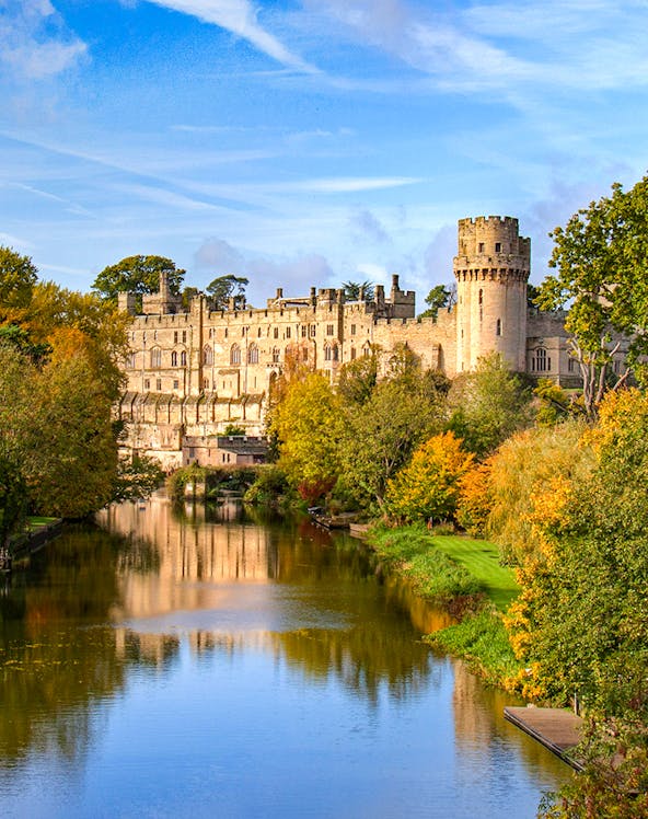 Warwick Castle with river reflection and autumn trees in Warwick, England.