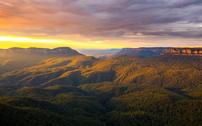 Blue Mountains Australia landscape at sunset with forested hills and distant cliffs.
