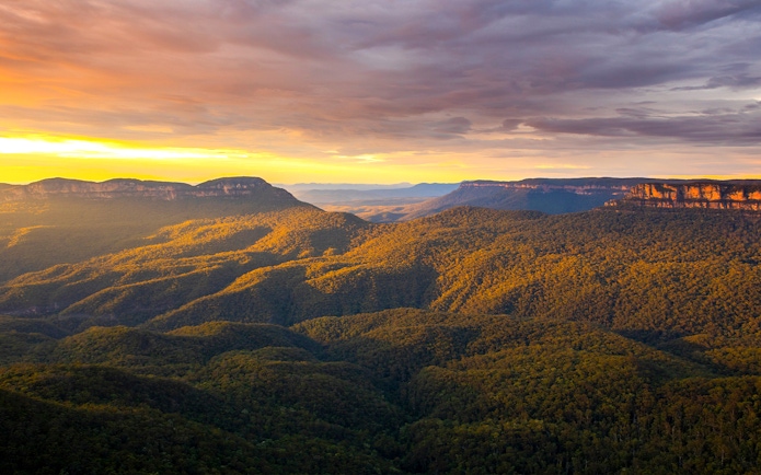 Blue Mountains Australia landscape at sunset with forested hills and distant cliffs.