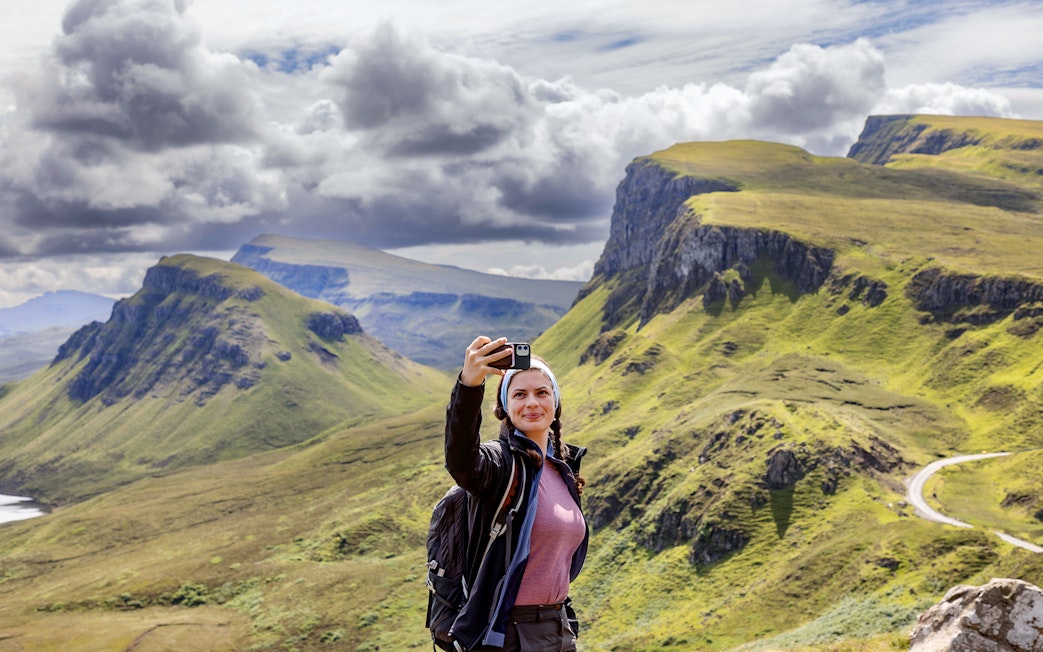 Traveler taking a selfie with the Quiraing mountains in the Isle of Skye, Scotland.