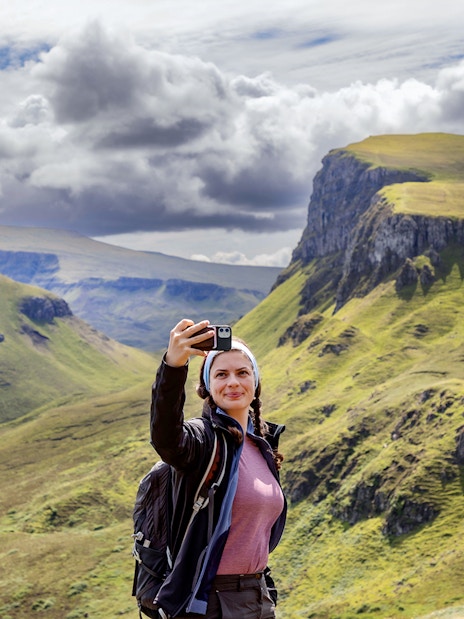 Traveler taking a selfie with the Quiraing mountains in the Isle of Skye, Scotland.