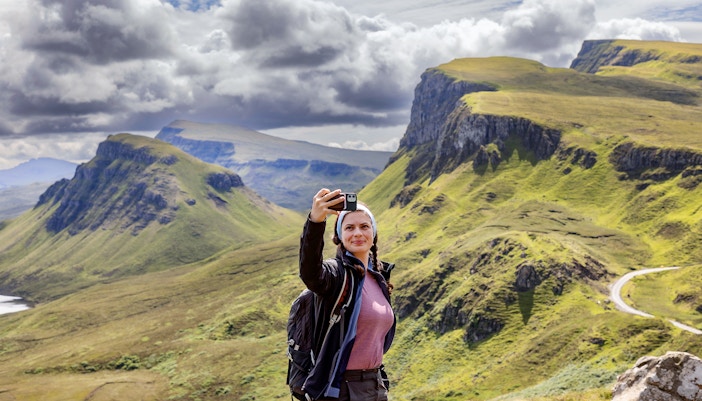 Traveler taking a selfie with the Quiraing mountains in the Isle of Skye, Scotland.
