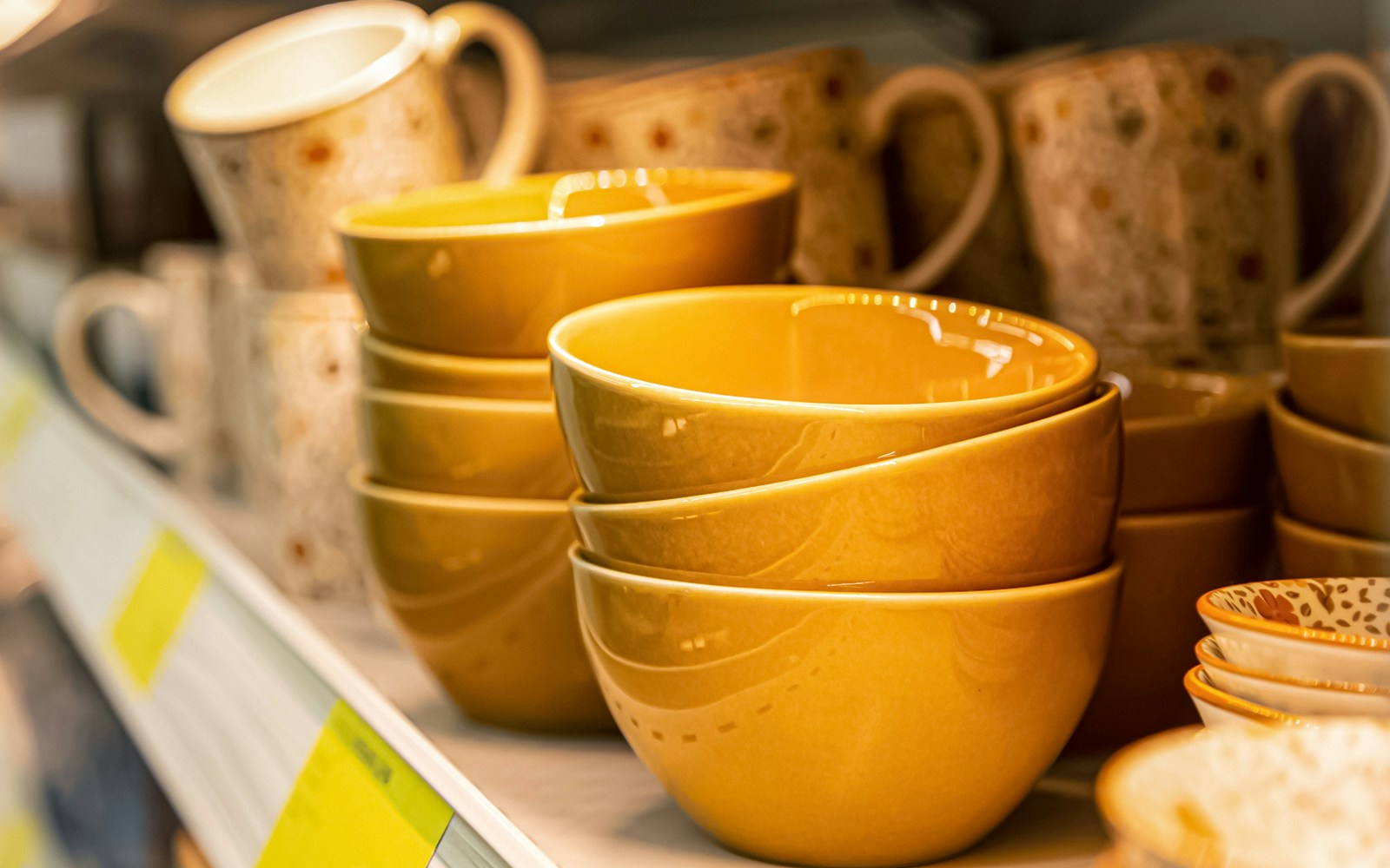 Stacked yellow ceramic bowls and patterned cups on a shelf.