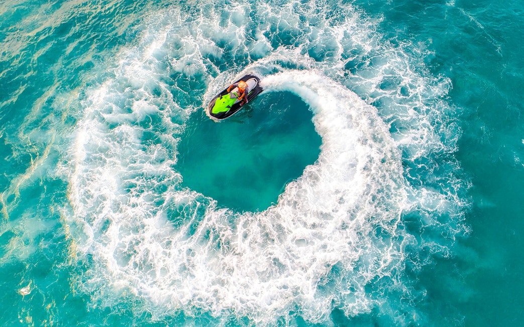 Aerial view of a person riding a jet ski in a circular motion on turquoise water.