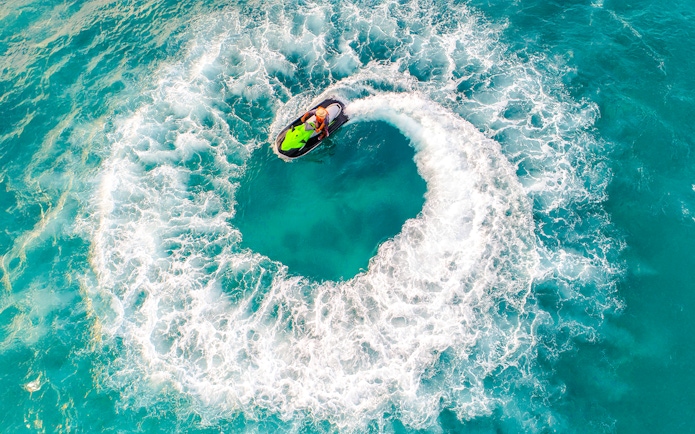 Aerial view of a person riding a jet ski in a circular motion on turquoise water.