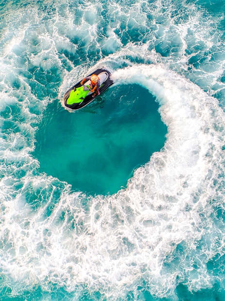 Aerial view of a person riding a jet ski in a circular motion on turquoise water.