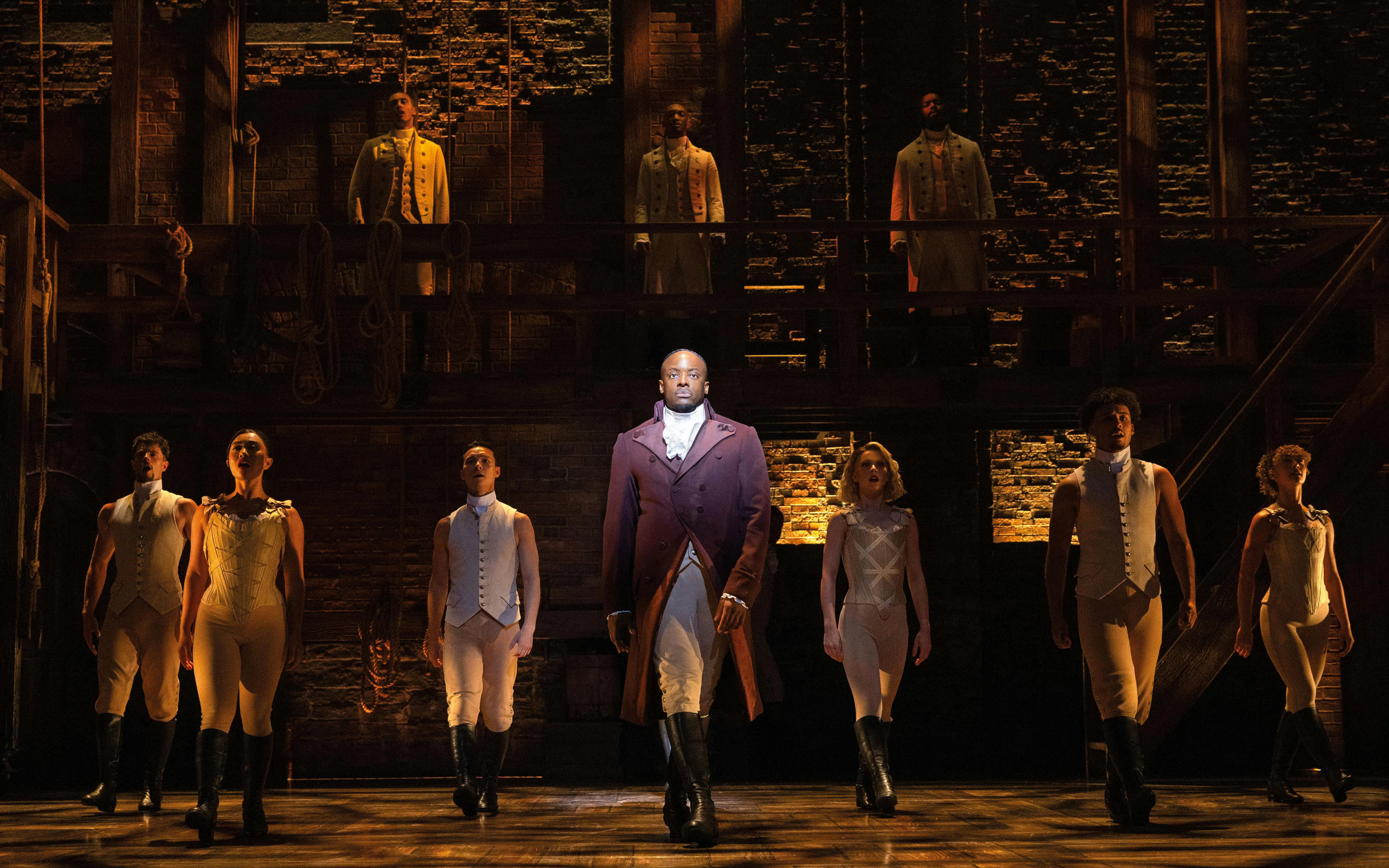 Cast performing Hamilton on West End stage, actors in period costumes.