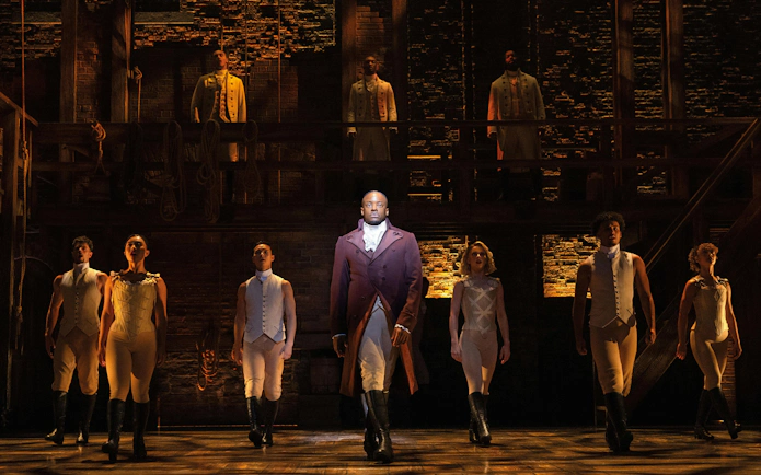 Cast performing Hamilton on West End stage, actors in period costumes.