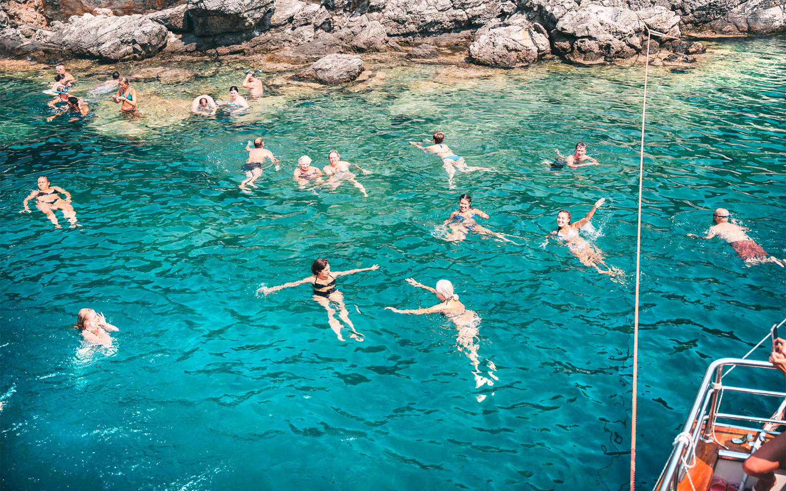 People swimming in clear blue waters near rocky shore during Blue Lagoon & Papanikolis Cruise.