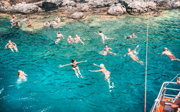 People swimming in clear blue waters near rocky shore during Blue Lagoon & Papanikolis Cruise.