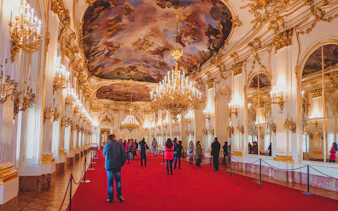 Visitors inside Schönbrunn Palace admiring ornate chandeliers and ceiling paintings.