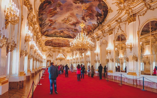 Visitors inside Schönbrunn Palace admiring ornate chandeliers and ceiling paintings.