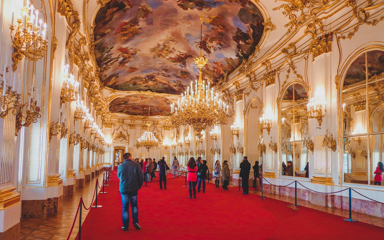 Visitors inside Schönbrunn Palace admiring ornate chandeliers and ceiling paintings.