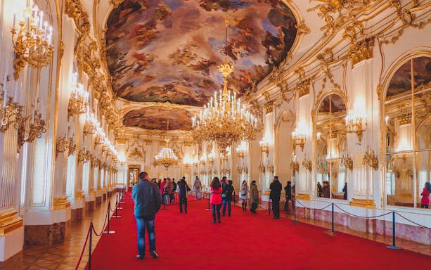 Visitors inside Schönbrunn Palace admiring ornate chandeliers and ceiling paintings.