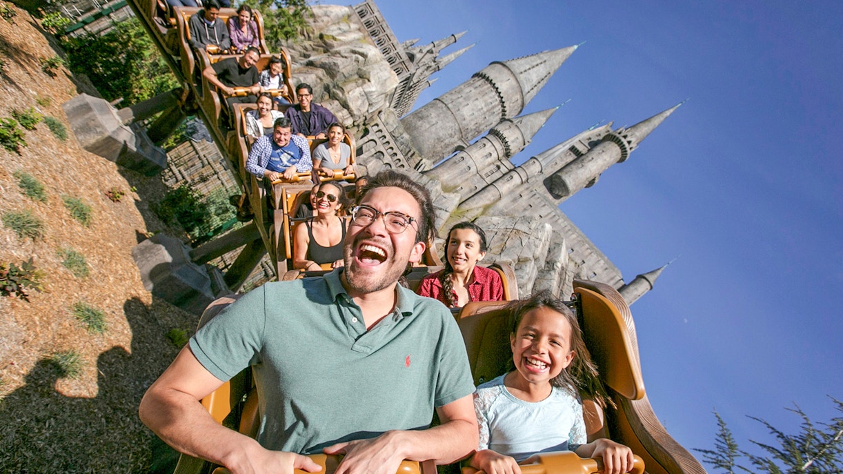Tourists enjoying a roller coaster ride at Universal Studios Hollywood with Hogwarts Castle in the background.